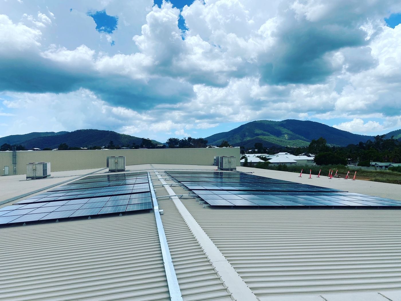 Rows of solar panels on a large commercial roof with green hills behind