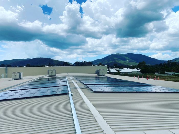 Two solar arrays on a wide commercial roof under a cloudy sky